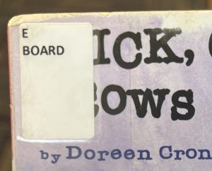 A closeup of the board book "Click, Clack, Moo: Cows That Type" focused on the spine label in the upper left corner of the cover that reads "E BOARD."