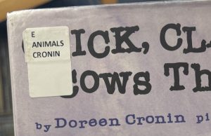 A closeup of the picture book "Click, Clack, Moo: Cows That Type" focused on the spine label in the upper left corner of the cover. The spine label reads "E ANIMALS CRONIN."