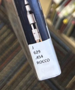 A closeup of the spine of the book "How We Got to the Moon" focused on the spine label. The spine label reads "J 629.454 ROCCO."