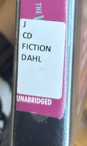 A closeup of the spine of the audiobook "The Witches," focusing on the spine label. The spine label reads "J CD FICTION DAHL."