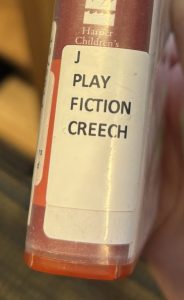 A closeup of the spine of the audiobook "Ruby Holler," focusing on the spine label. The spine label reads "J PLAY FICTION CREECH."