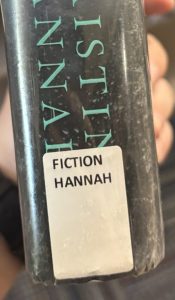 A closeup of the spine on the book "The Nightingale," focusing on the spine label. The spine label reads "FICTION HANNAH."