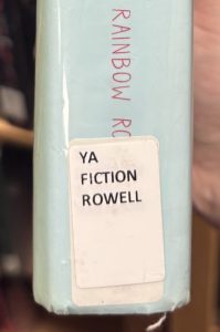A closeup of the spine on the book "Fangirl," focusing on the spine label. The spine label reads "YA FICTION ROWELL."
