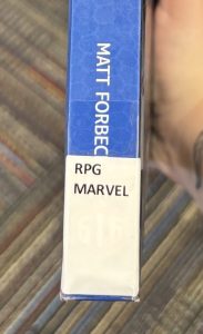 A closeup of the spine on the book "Marvel Multiverse Role-Playing Game Core Rulebook," focusing on the spine label. The spine label reads "RPG MARVEL."