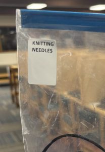 A closeup of the spine label given to a bag holding various knitting needles. The spine label reads "KNITTING NEEDLES."