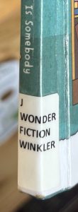 A closeup of the spine of the Wonderbook "Here's Hank," focusing on the spine label. The spine label reads "J WONDER FICTION WINKLER."